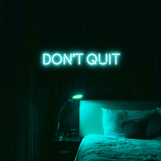 Don't Quit LED Neon Light Sign in turquoise, featuring block lettering illuminated above a bed.