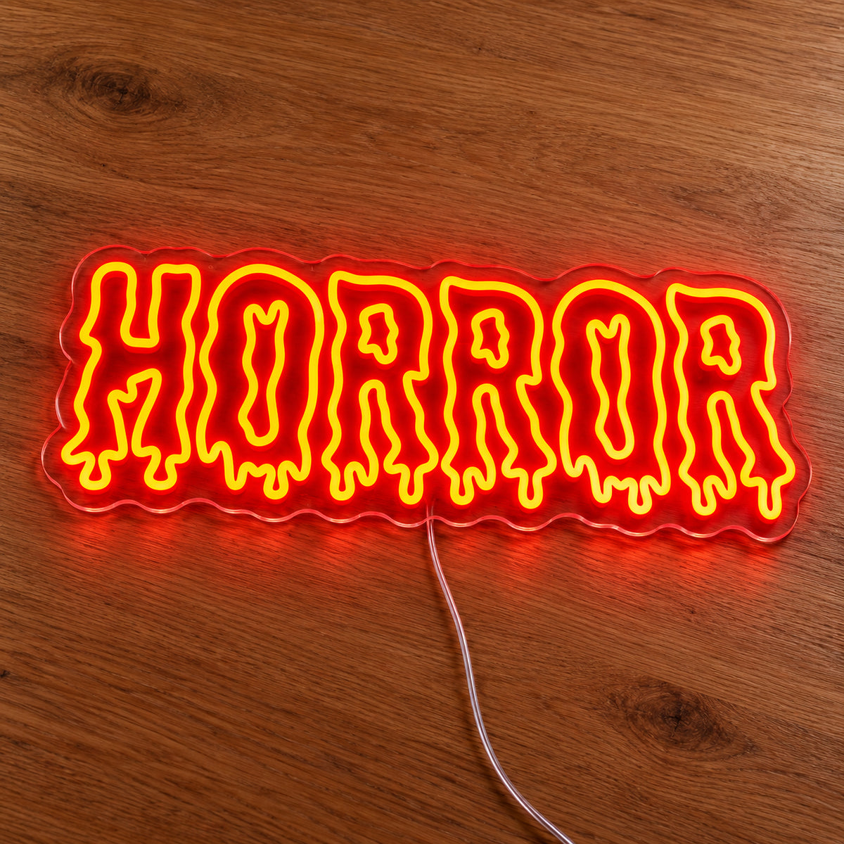 Horror Dripping Letters Neon Sign featuring the word Horror in orange outlined letters with dripping edges, illuminated on clear acrylic lying on a natural oak wooden surface.