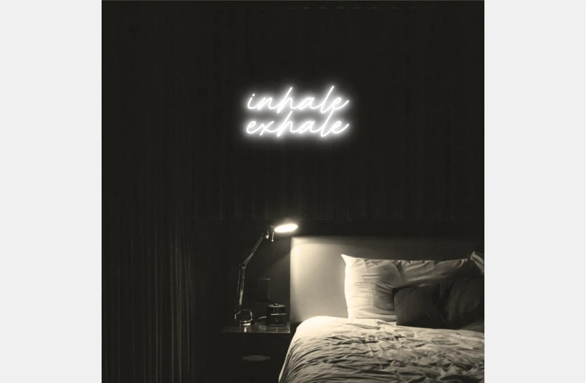 Inhale Exhale LED Neon Light Sign in white, featuring two lines of script lettering illuminated above a bed.