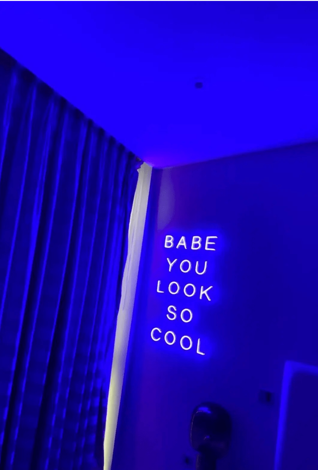 Babe You Look So Cool 2 LED Neon Light Sign in purple, featuring five stacked words on a bedroom wall beside curtains.