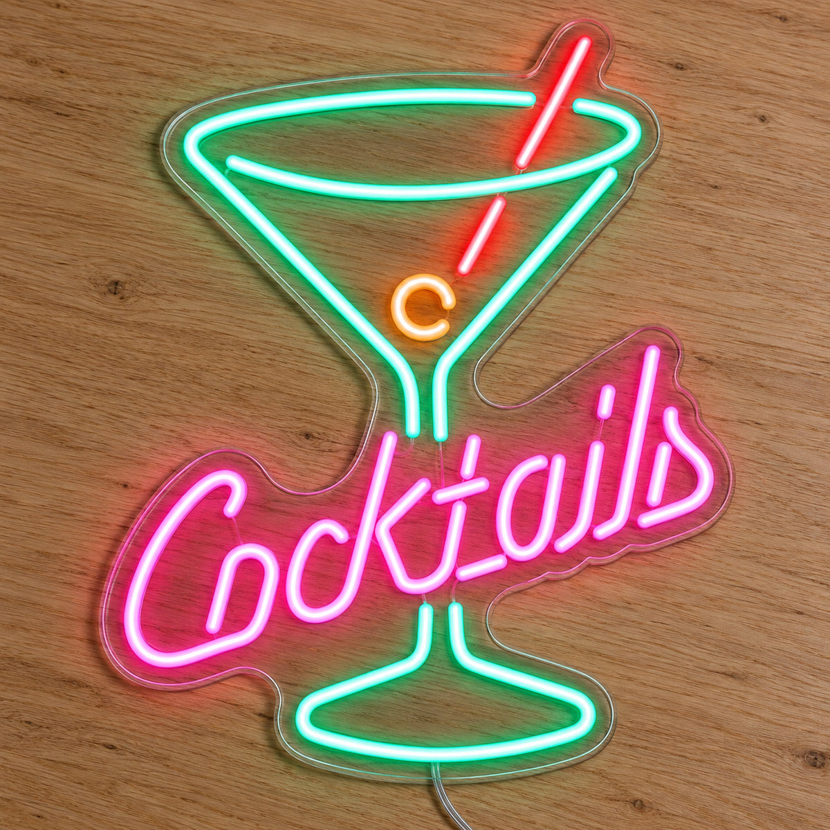 Cocktails Glass LED Neon Sign - Bar and Venue Icon Sign in pink, green and orange, featuring a cocktail-glass outline above Cocktails lettering on a wooden surface.