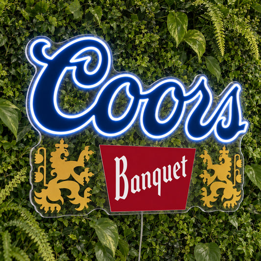 Coors Banquet LED Neon Sign, featuring illuminated beer-brand logo on a green foliage wall.