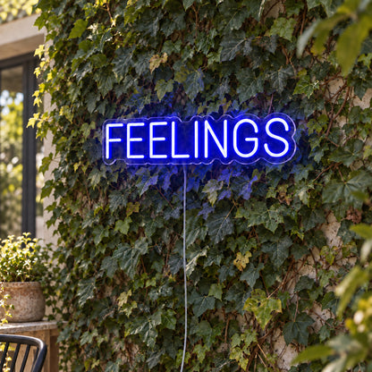 Feelings Neon Sign in blue, featuring block lettering against a foliage wall.