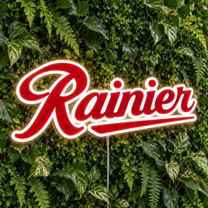 Rainier LED Neon Sign, featuring illuminated beer-brand logo on a green foliage wall.