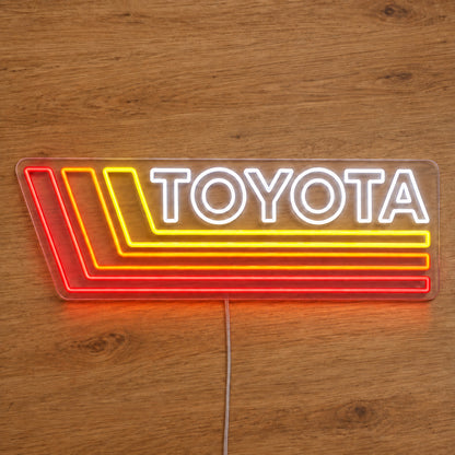 Toyota Retro Land Cruiser LED Neon Sign in white, red and yellow, featuring Toyota lettering with retro stripes on a wooden surface.
