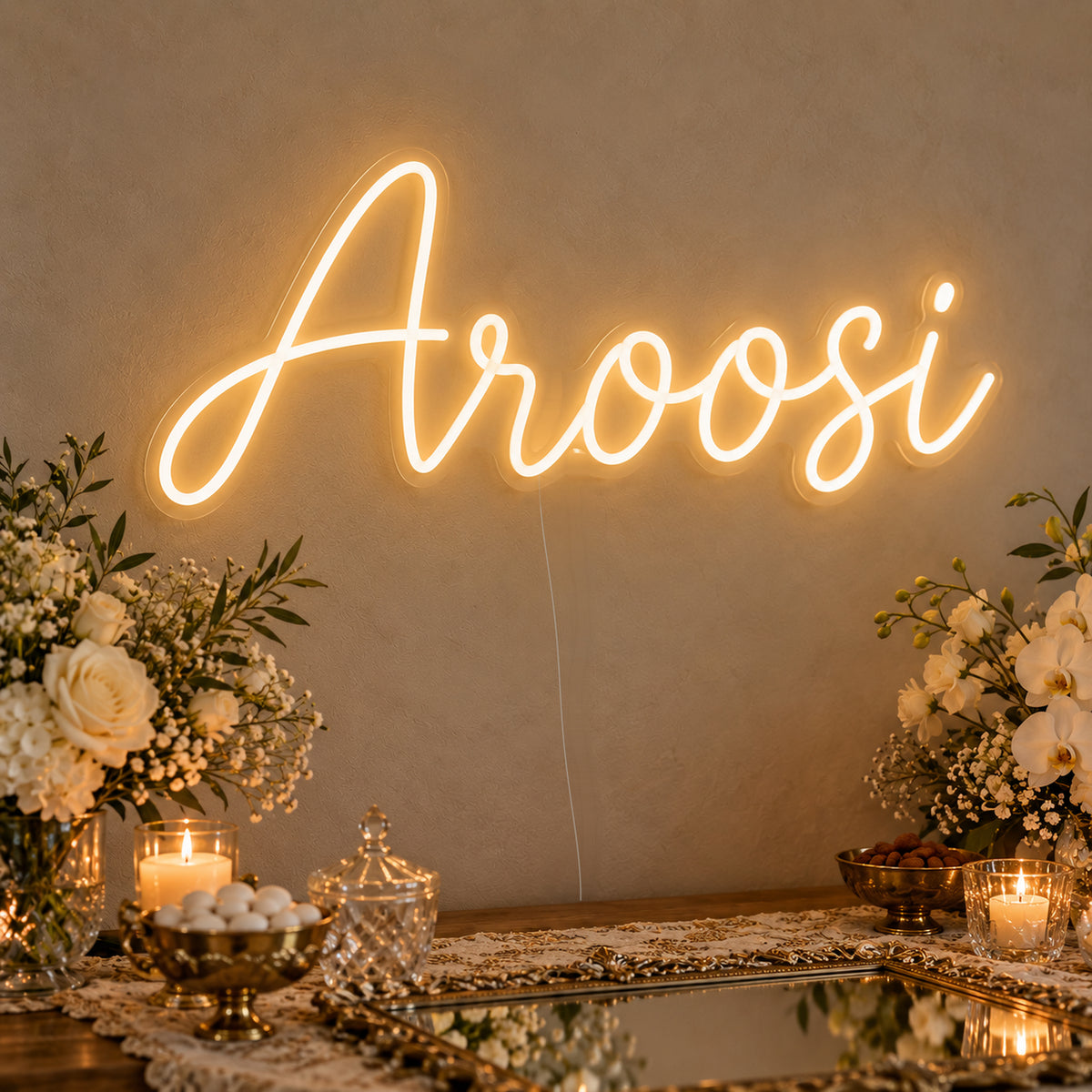 Aroosi Neon Sign on clear cut-to-shape acrylic, illuminated on a wall in a styled celebration setting