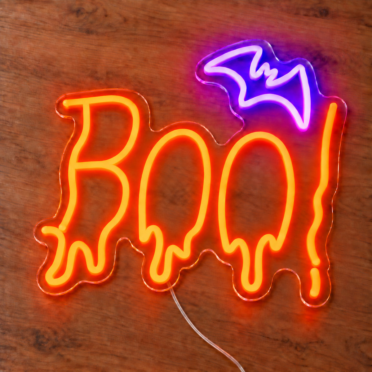 Boo Bat Neon Sign featuring orange dripping Boo lettering topped with a purple bat, illuminated on clear acrylic lying on a natural oak wooden surface.