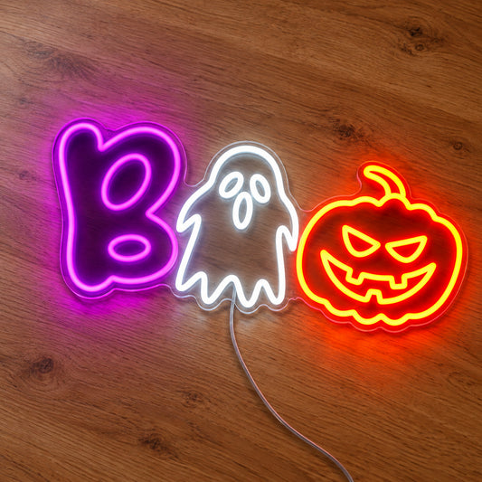 Boo Ghost and Pumpkin Neon Sign featuring a purple B, a white ghost and an orange pumpkin arranged to spell Boo, illuminated on clear acrylic lying on a natural oak wooden surface.
