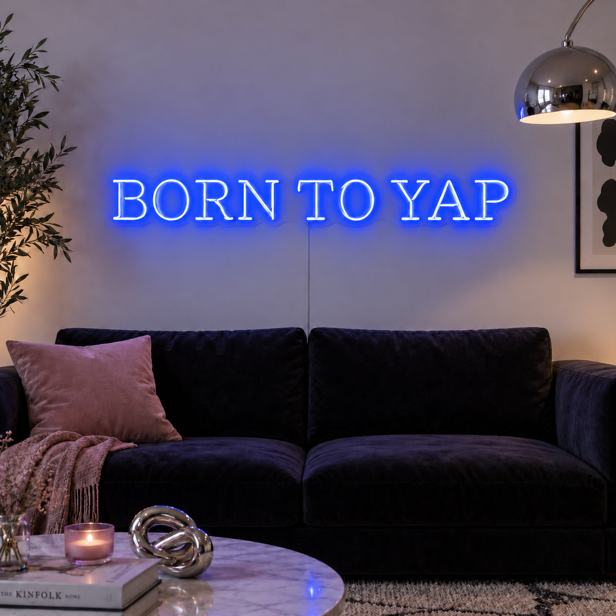 Born To Yap Neon Sign glowing blue above a dark sofa and glass coffee table.