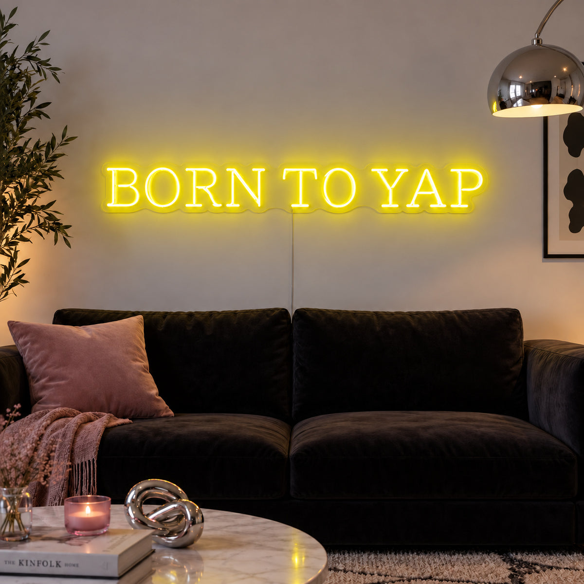 Born To Yap Neon Sign with yellow lighting, displayed above a dark sofa and glass coffee table.