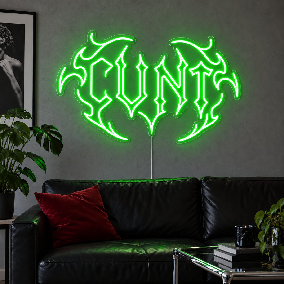 Cunt Neon Sign with green lighting, displayed in a tribal design above a black leather sofa.