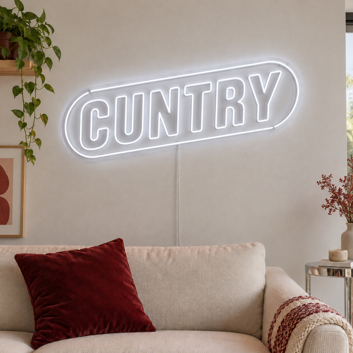 Cuntry Neon Sign glowing white inside a rounded border above a cream sofa.