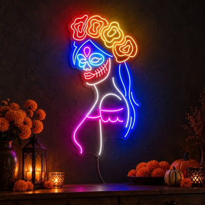 Day of the Dead Woman Neon Sign featuring a woman in profile with a decorative skull face, blue hair, a floral crown and pink accents, glowing on a dark wall in a Halloween room display.
