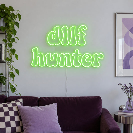 DILF Hunter Neon Sign in green above a sofa with purple cushions.