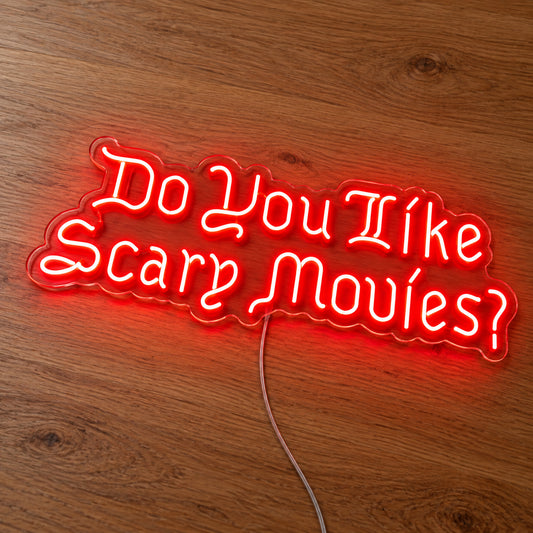 Do You Like Scary Movies Neon Sign featuring the question Do You Like Scary Movies in decorative red lettering, illuminated on clear acrylic lying on a natural oak wooden surface.