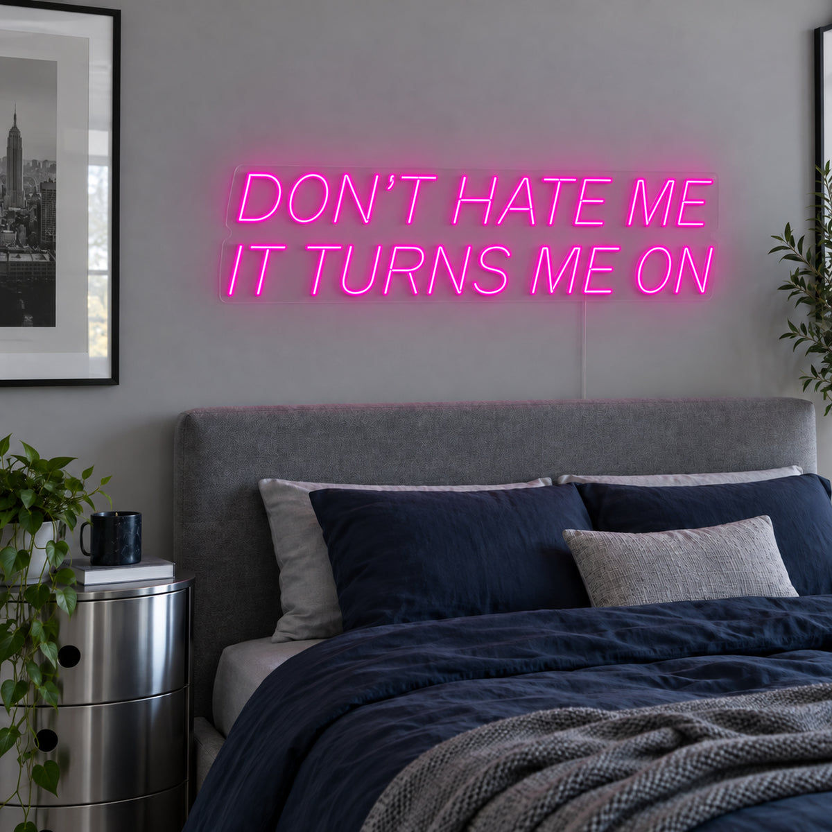 Don't Hate Me It Turns Me On Neon Sign in rose red above a bed with dark blue bedding.
