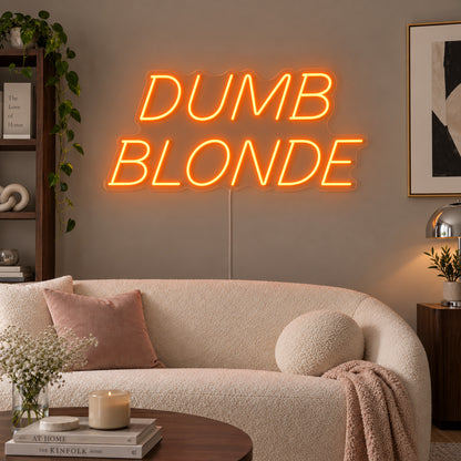 Orange version of the Dumb Blonde Neon Sign, shown in slanted lettering above a cream sofa.