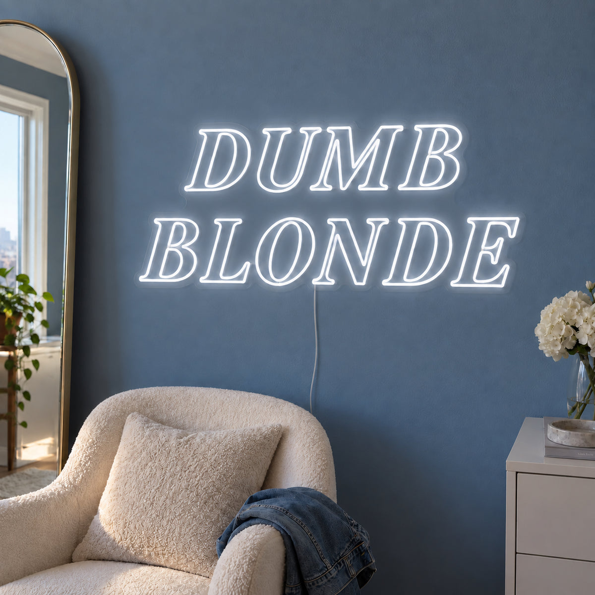 Dumb Blonde Neon Sign, RGB colour-changing option shown in white in outlined serif lettering above a cream chair.