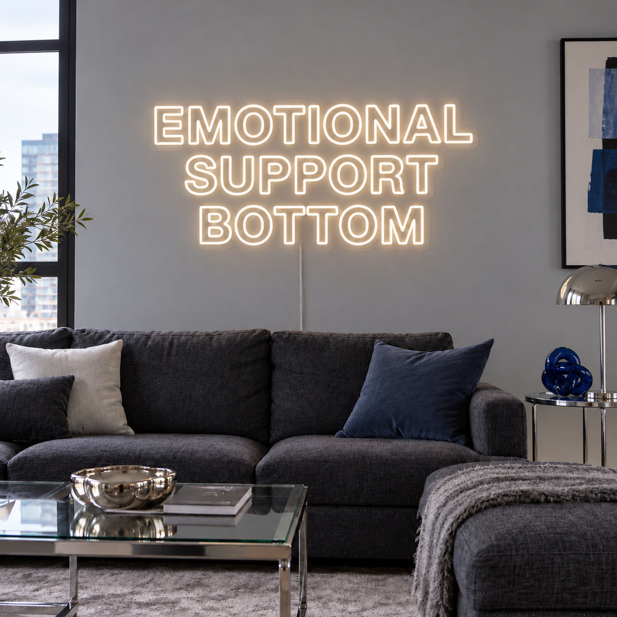 Warm White version of the Emotional Support Bottom Neon Sign, shown above a charcoal sofa.