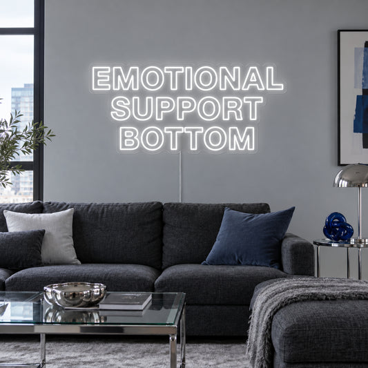 Emotional Support Bottom Neon Sign in white above a charcoal sofa.