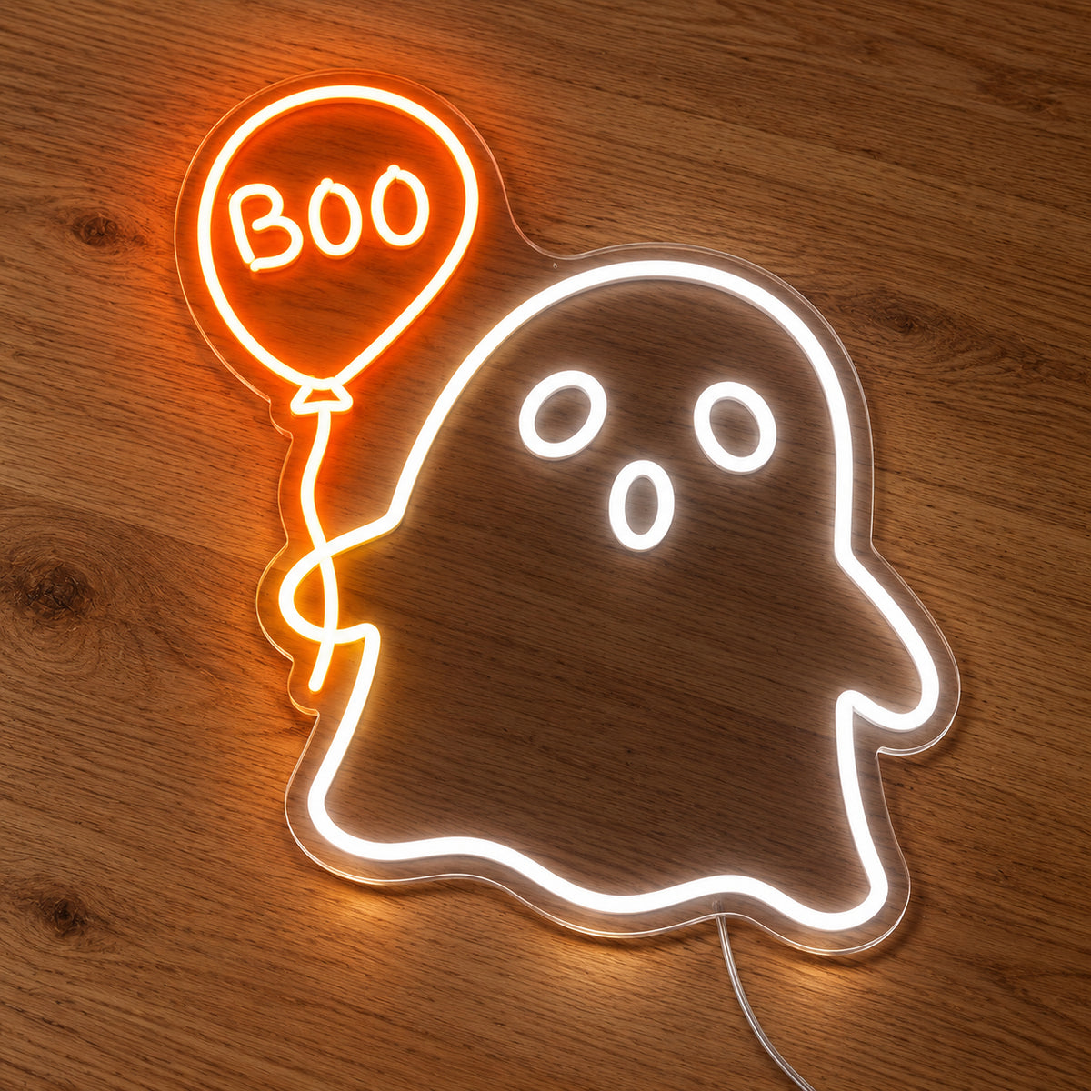 Ghost with Boo Balloon Neon Sign featuring a white ghost holding an orange balloon with Boo lettering, illuminated on clear acrylic lying on a natural oak wooden surface.