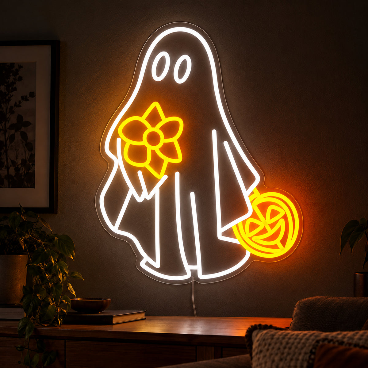 Ghost with Flower and Pumpkin Neon Sign featuring a white ghost holding a yellow flower and an orange pumpkin shaped bucket, displayed on a dark wall above a wooden sideboard.