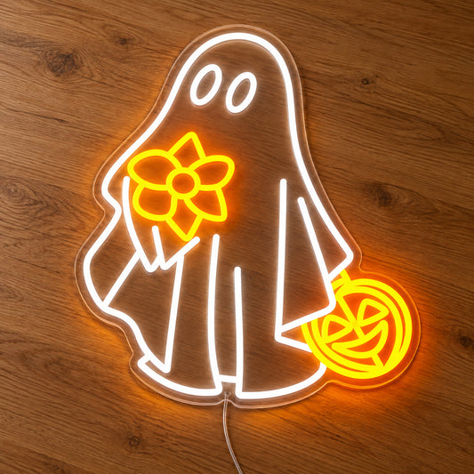 Ghost with Flower and Pumpkin Neon Sign featuring a white ghost holding a yellow flower and an orange pumpkin shaped bucket, illuminated on clear acrylic lying on a natural oak wooden surface.