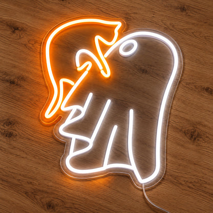 Ghost with Witch Hat Neon Sign featuring a white ghost wearing a floppy orange witch hat, illuminated on clear acrylic lying on a natural oak wooden surface.
