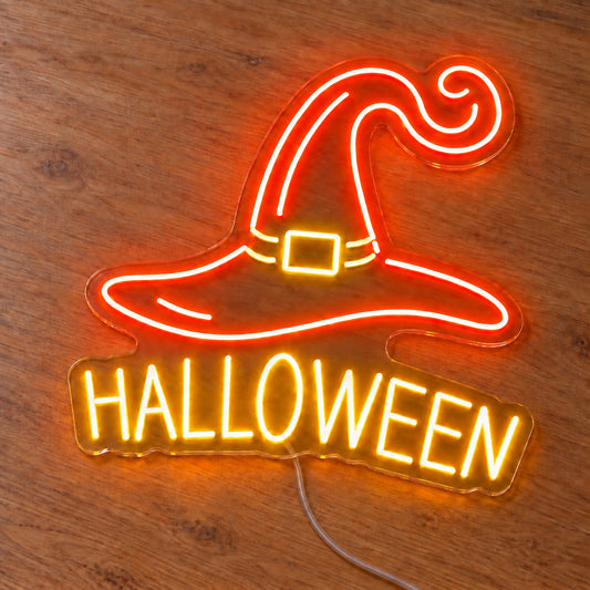 Halloween Witch Hat Neon Sign featuring an orange witch hat with a curled tip above Halloween lettering, illuminated on clear acrylic lying on a natural oak wooden surface.