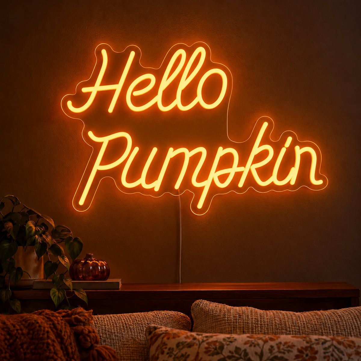 Hello Pumpkin Orange Neon Sign featuring Hello Pumpkin wording in flowing orange script over two lines, displayed on a dark wall above a wooden sideboard.