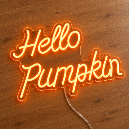 Hello Pumpkin Orange Neon Sign featuring Hello Pumpkin wording in flowing orange script over two lines, illuminated on clear acrylic lying on a natural oak wooden surface.
