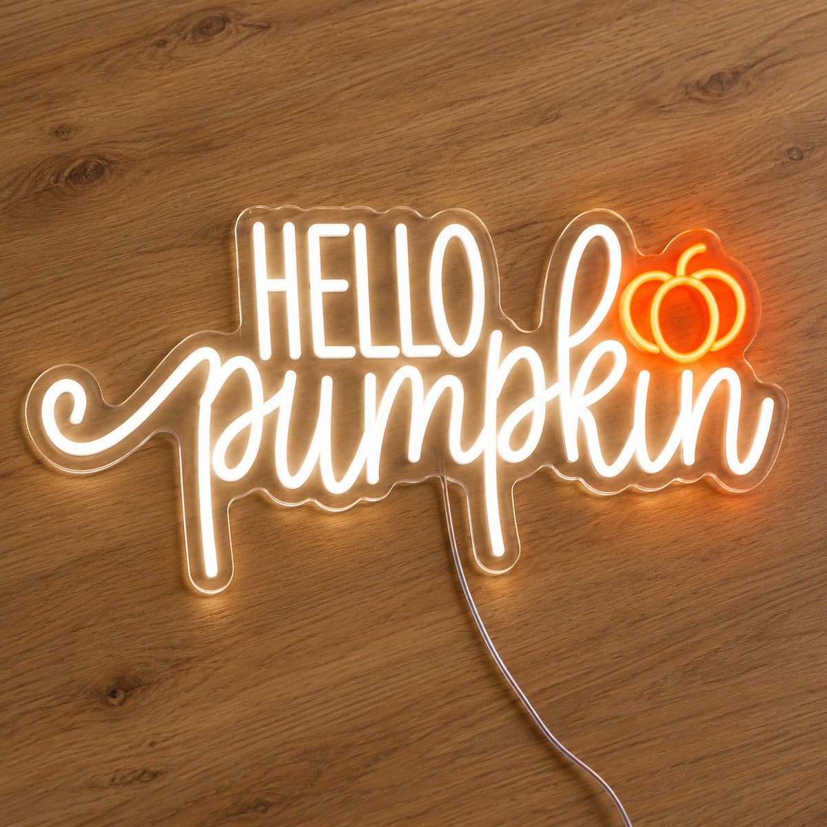 Hello Pumpkin White Neon Sign featuring white Hello Pumpkin lettering with flowing script and a small orange pumpkin, illuminated on clear acrylic lying on a natural oak wooden surface.