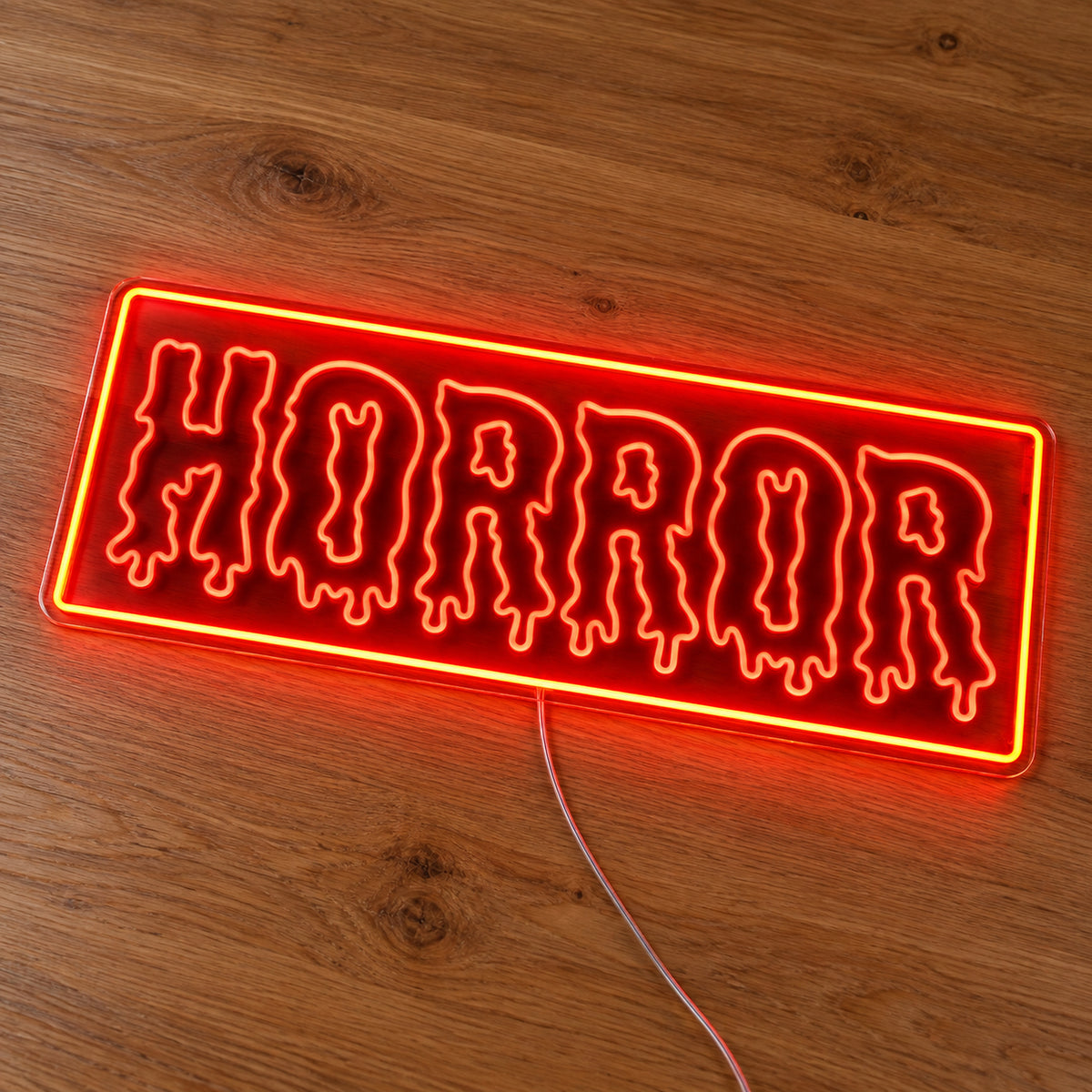 Horror Rectangle Neon Sign featuring dripping Horror lettering inside an orange rectangular border, illuminated on clear acrylic lying on a natural oak wooden surface.