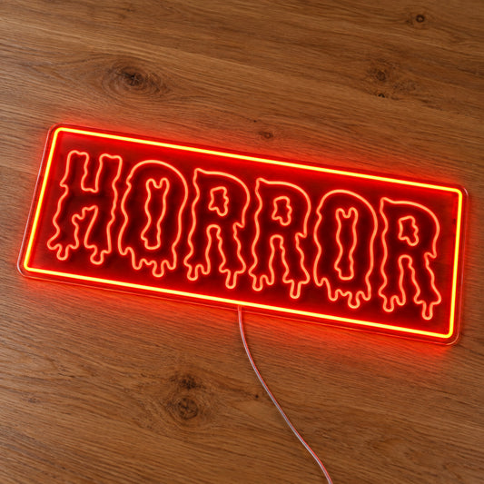 Horror Rectangle Neon Sign featuring dripping Horror lettering inside an orange rectangular border, illuminated on clear acrylic lying on a natural oak wooden surface.