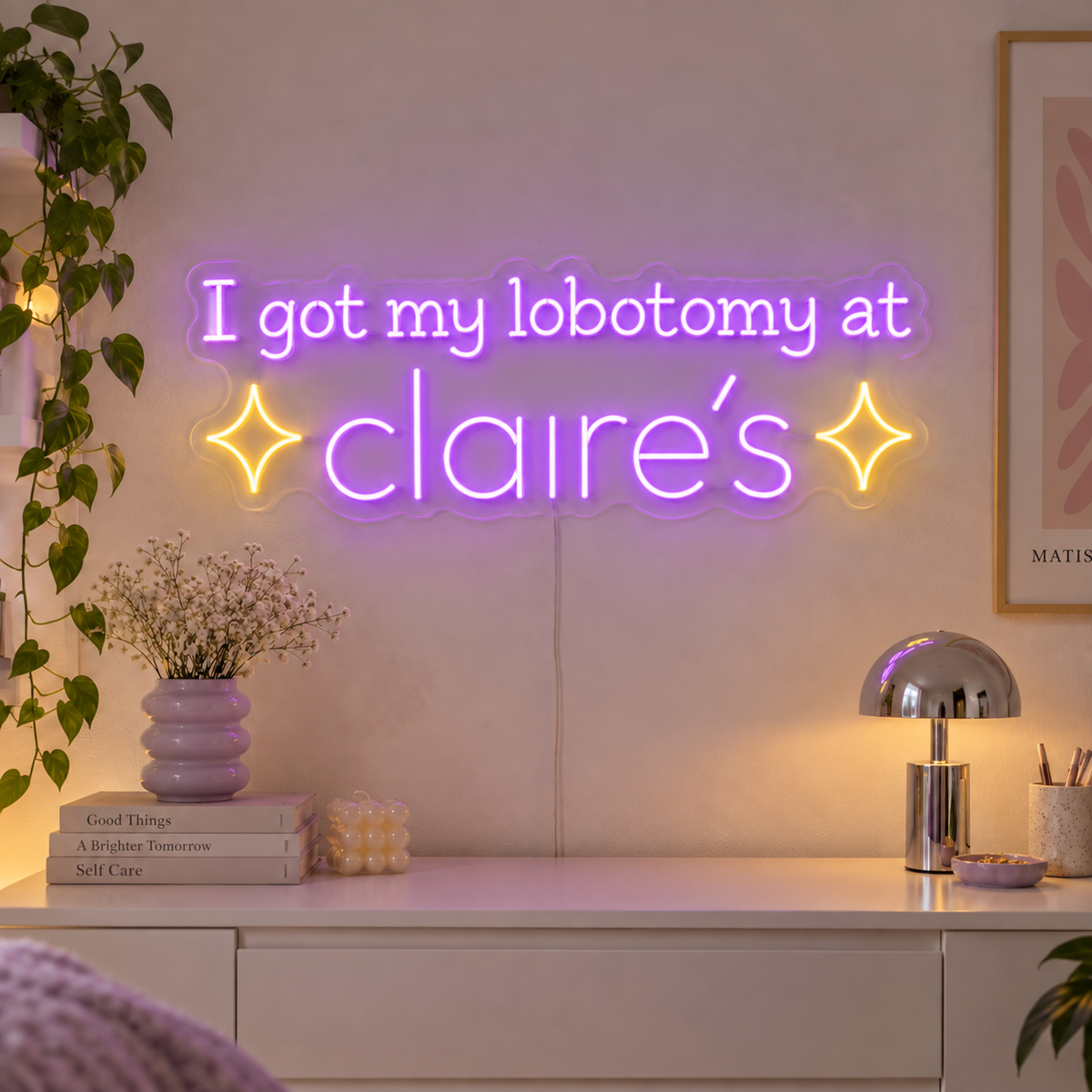 I Got My Lobotomy At Claire's Neon Sign with purple lettering with two yellow sparkle shapes on transparent acrylic, displayed on a living room wall