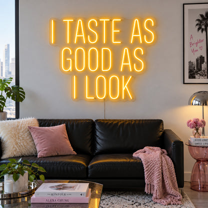 I Taste As Good As I Look Neon Sign glowing gold above a black sofa.