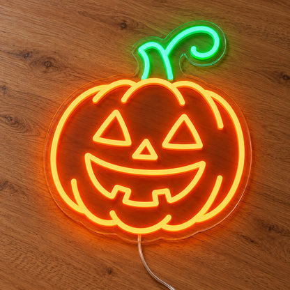 Jack O Lantern Neon Sign featuring an orange pumpkin with triangular eyes, a smiling mouth and a green stem, illuminated on clear acrylic lying on a natural oak wooden surface.