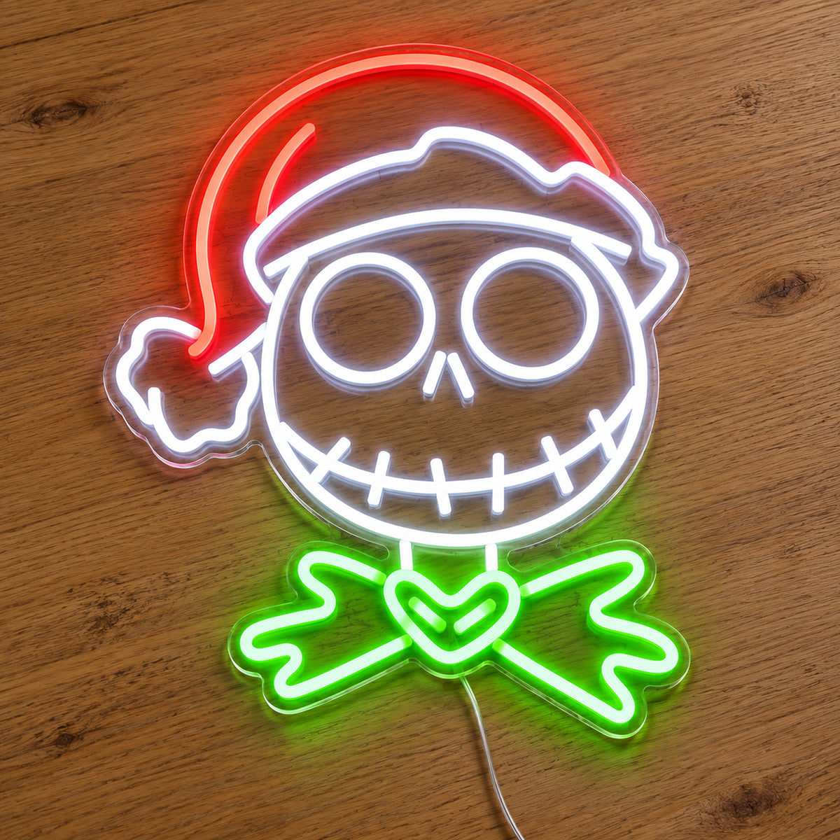 Jack Skellington Santa Hat Neon Sign featuring a white stitched skull face, a red Santa hat and green bow details, illuminated on clear acrylic lying on a natural oak wooden surface.