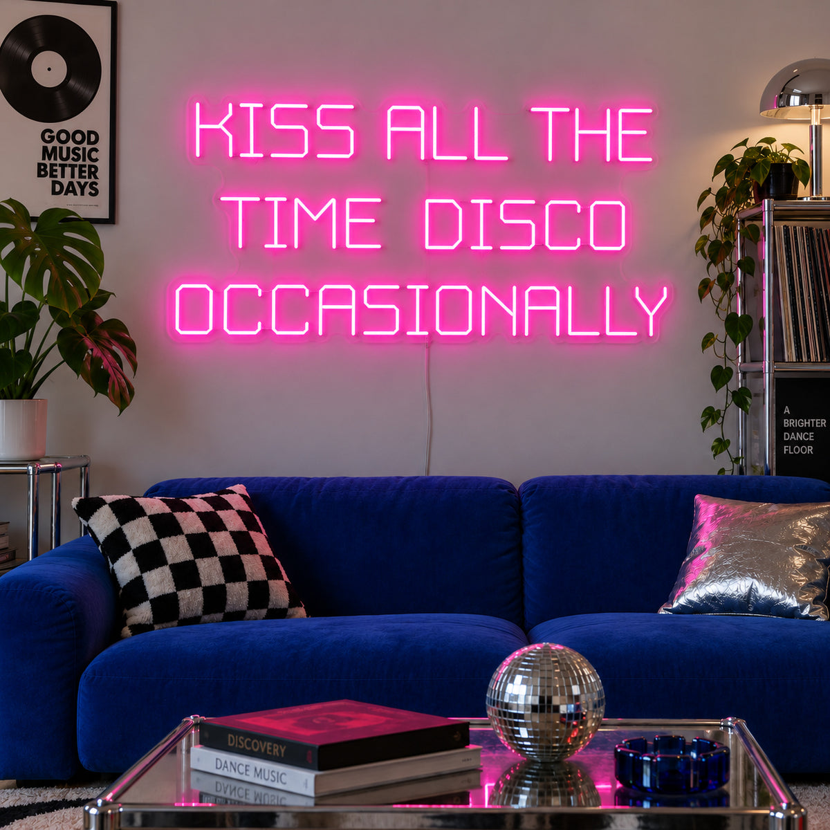 Kiss All The Time Disco Occasionally Neon Sign glowing pink above a blue sofa near a disco ball.