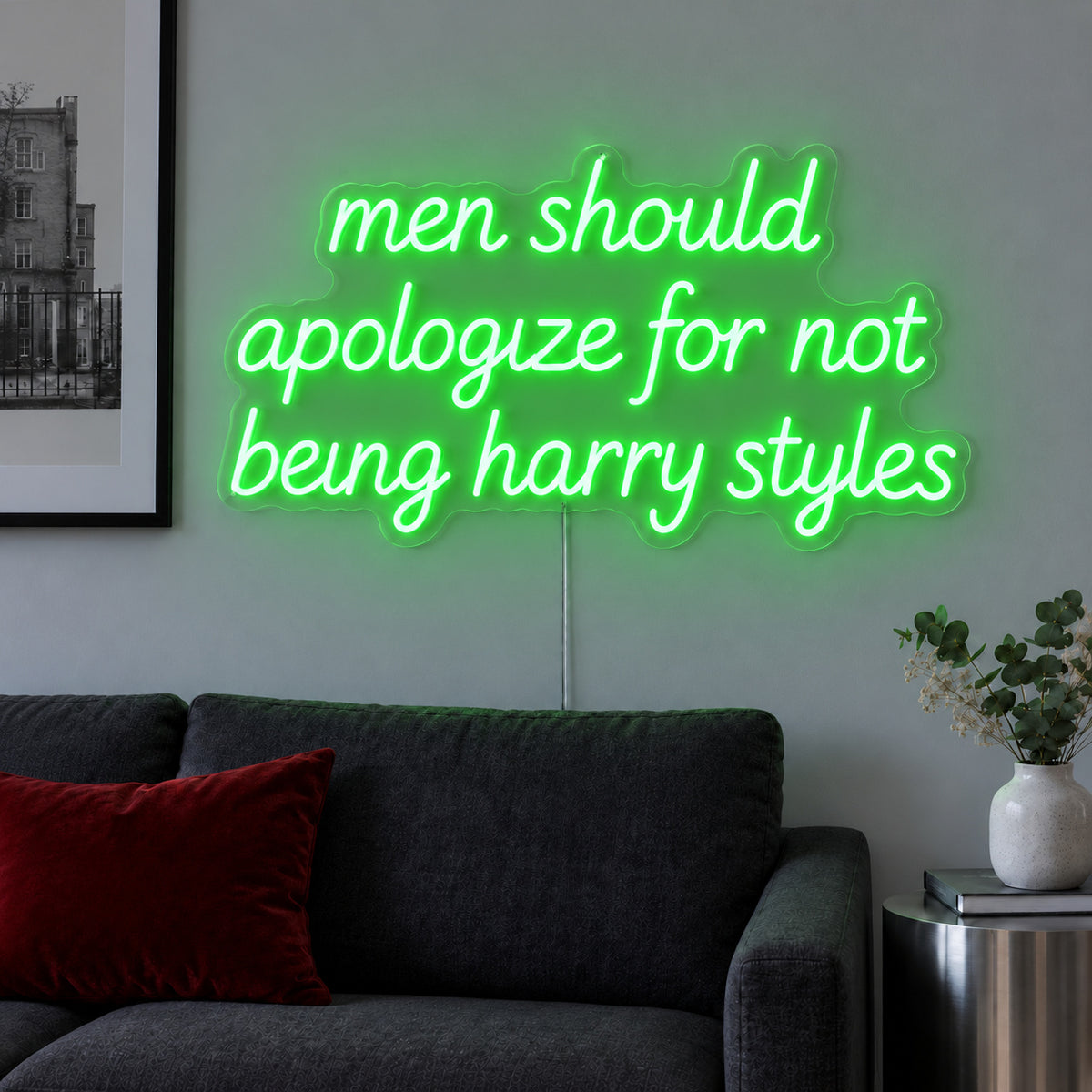 Men Should Apologize For Not Being Harry Styles Neon Sign with green lighting, displayed above a dark sofa.