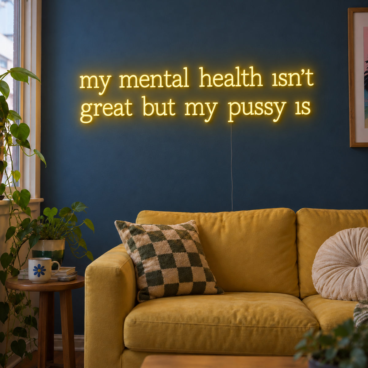 My Mental Health Isn't Great But My Pussy Is Neon Sign with warm yellow lettering arranged in two lines on transparent acrylic, displayed on a living room wall