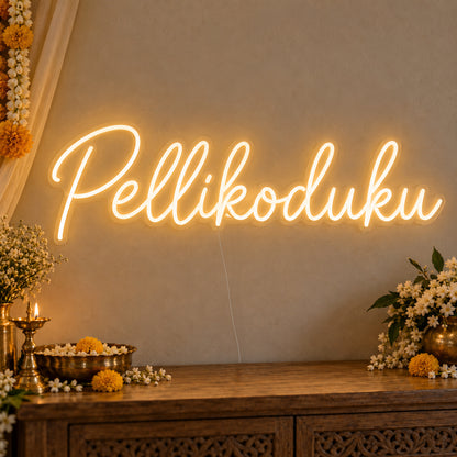 Pellikoduku Neon Sign on clear cut-to-shape acrylic, illuminated on a wall in a styled celebration setting
