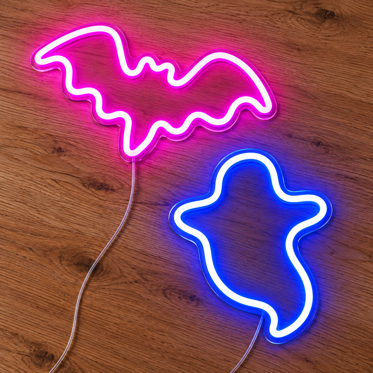 Pink Bat and Blue Ghost Neon Sign featuring a bright pink bat above a blue ghost outline, illuminated on clear acrylic lying on a natural oak wooden surface.