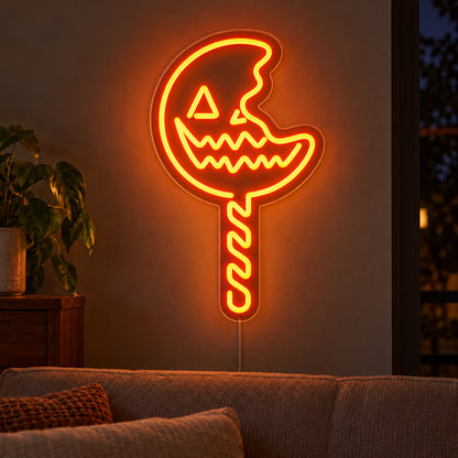 Pumpkin Lollipop Neon Sign featuring an orange jack o lantern lollipop with a bite shaped edge and a striped stick, glowing on a dark living room wall.
