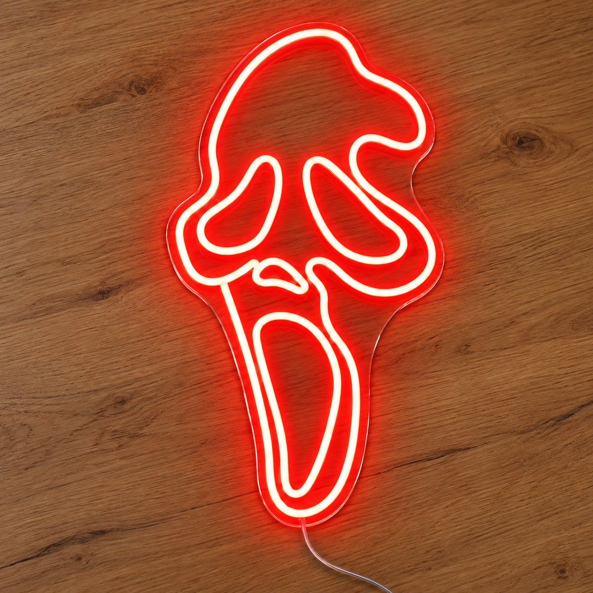 Red Ghostface Neon Sign featuring the Ghostface mask outlined in red, with elongated eyes and an open mouth, illuminated on clear acrylic lying on a natural oak wooden surface.