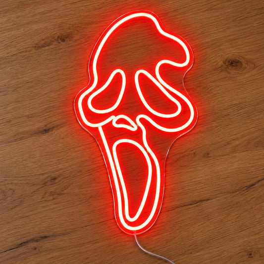 Red Ghostface Neon Sign featuring the Ghostface mask outlined in red, with elongated eyes and an open mouth, illuminated on clear acrylic lying on a natural oak wooden surface.