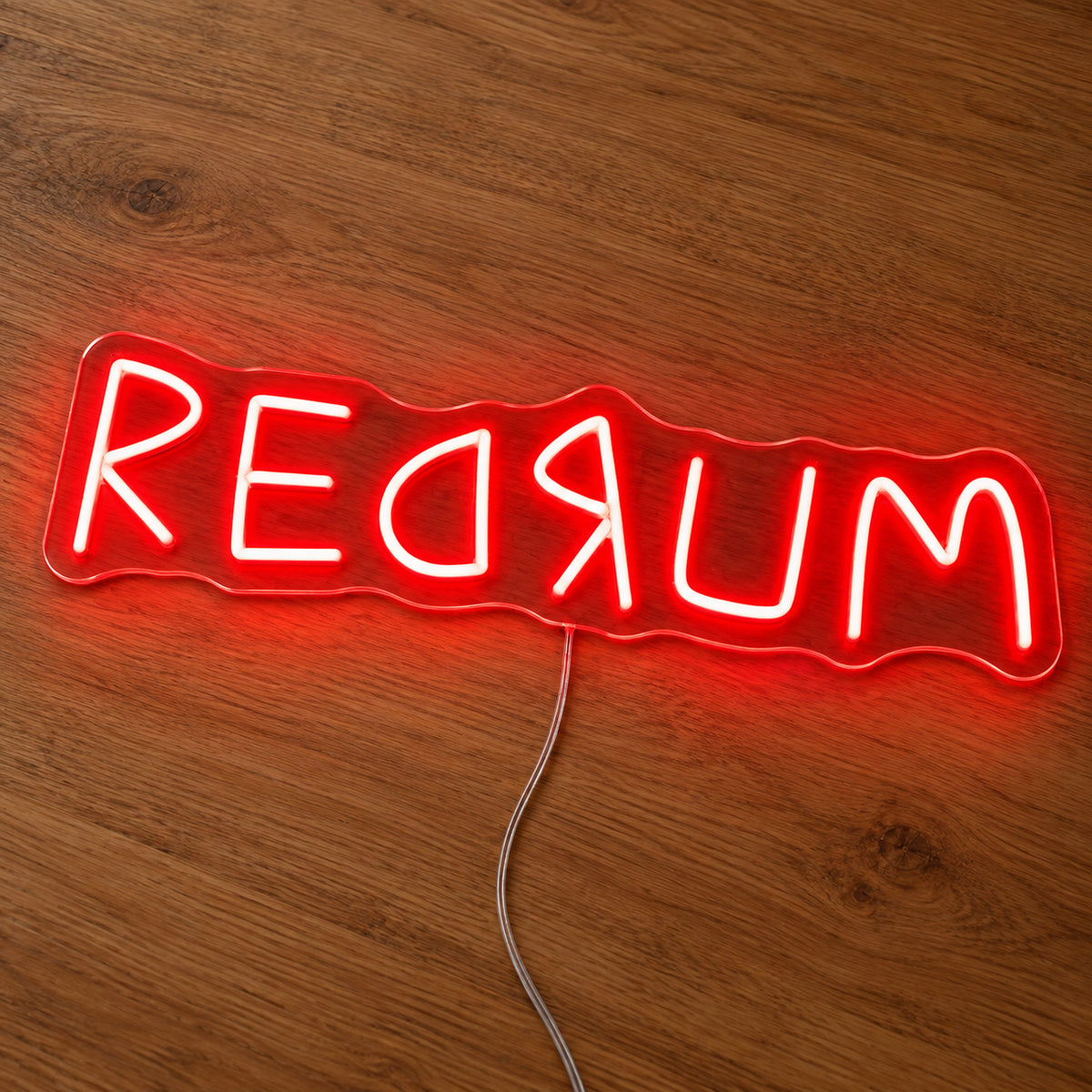 Redrum Neon Sign featuring red Redrum lettering with reversed letter details, illuminated on clear acrylic lying on a natural oak wooden surface.