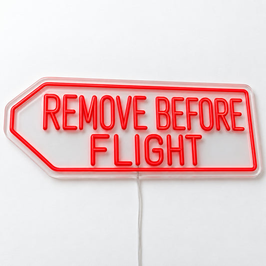 Remove Before Flight Neon Sign, featuring Remove Before Flight lettering inspired by aviation safety tags, on a single clear acrylic backing displayed on a white surface.
