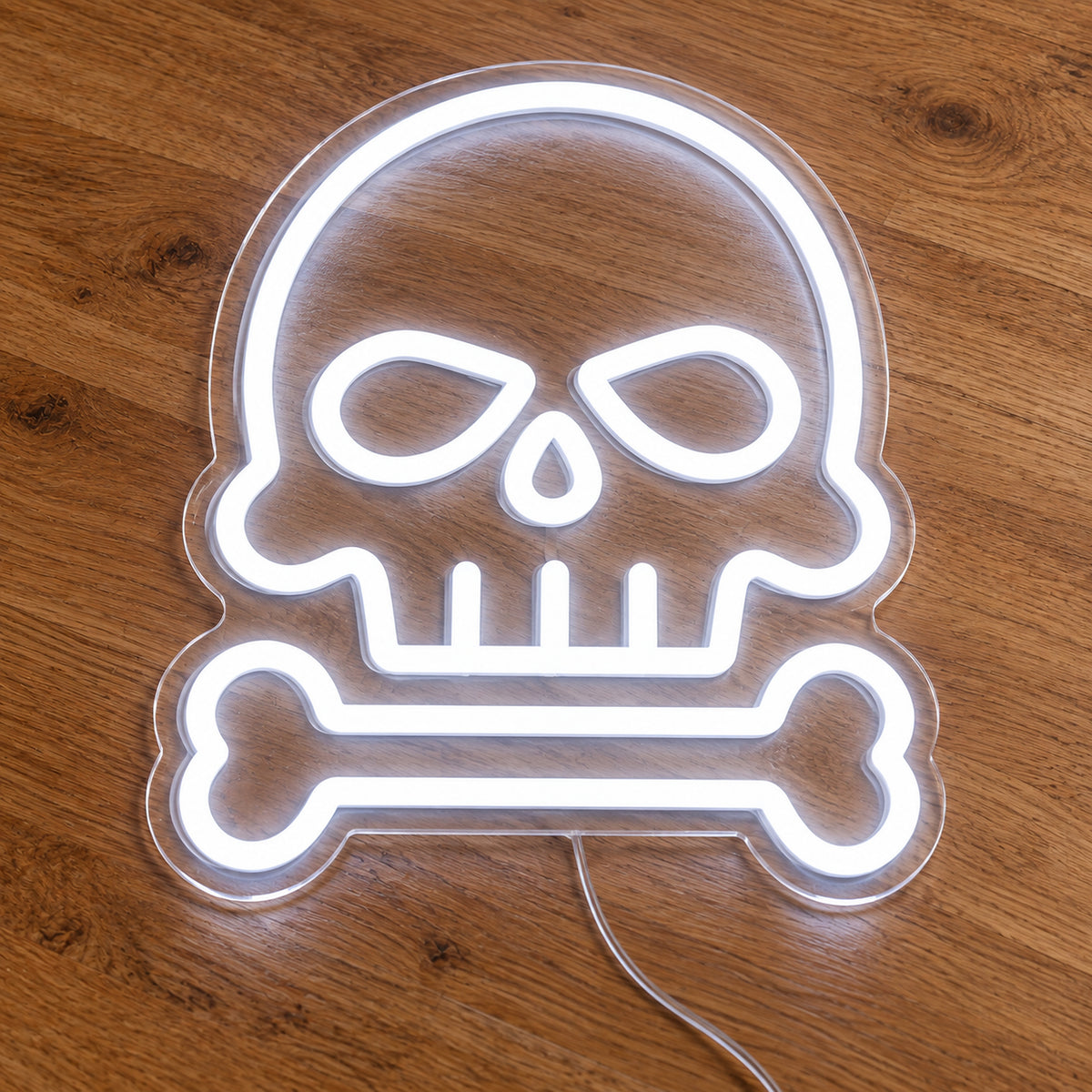 Skull and Bone Neon Sign featuring a white skull outline above a single horizontal bone, illuminated on clear acrylic lying on a natural oak wooden surface.