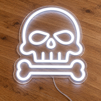 Skull and Bone Neon Sign featuring a white skull outline above a single horizontal bone, illuminated on clear acrylic lying on a natural oak wooden surface.